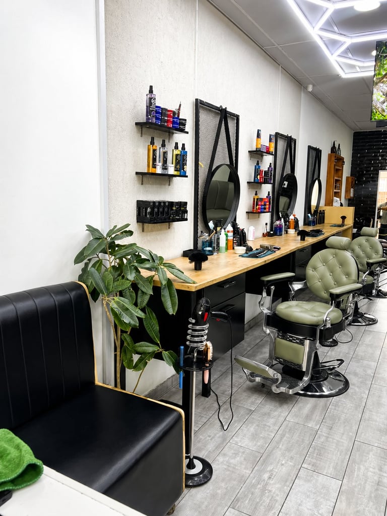 Modern barbershop interior with styling stations, black barber chairs, wall-mounted shelves with hair products, and decorative plants