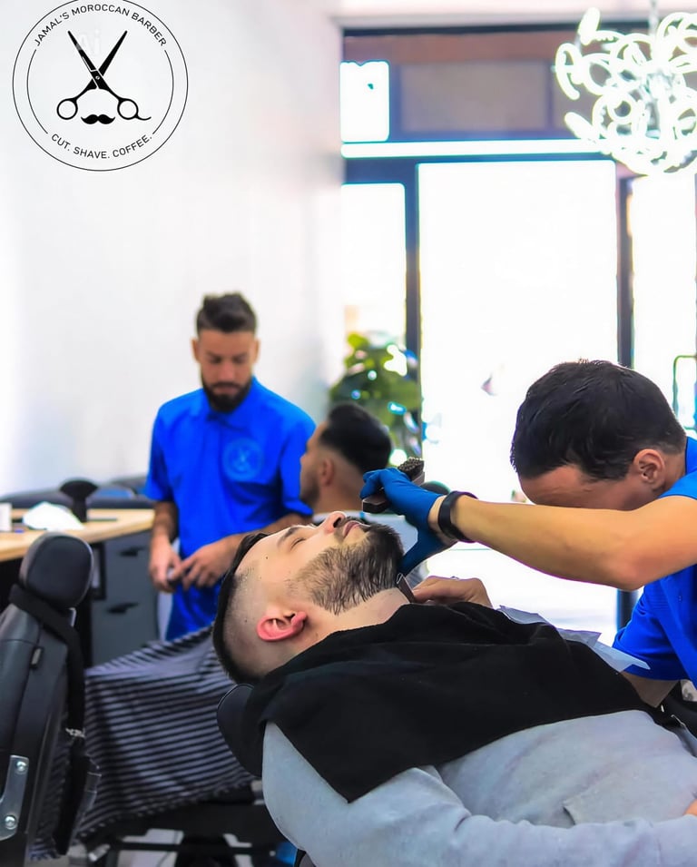 Barber giving a customer a haircut in a salon with blue-uniformed staff visible in the background